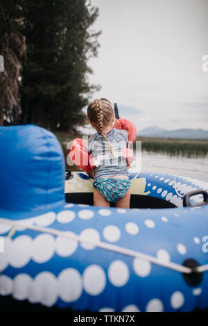 Vista posteriore della ragazza con ali di acqua in piedi in zattera gonfiabile sul lago Foto Stock