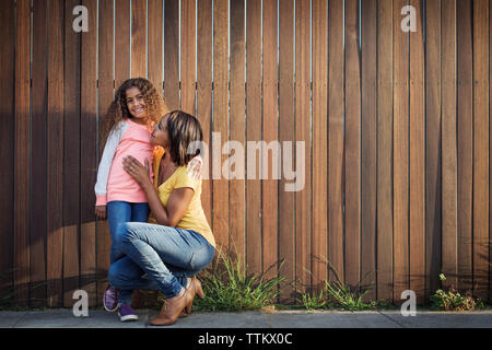 Madre abbracciando la figlia contro la recinzione di legno Foto Stock