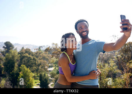 Coppia felice tenendo selfie attraverso il telefono cellulare sul campo Foto Stock