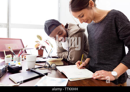 Maschio sorridente illustrator guardando collega la pittura alla scrivania in ufficio creativo Foto Stock