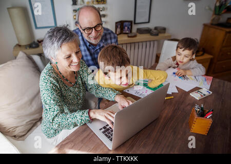 Angolo di alta vista di felice nonni e nipoti utilizzando portatile a casa Foto Stock