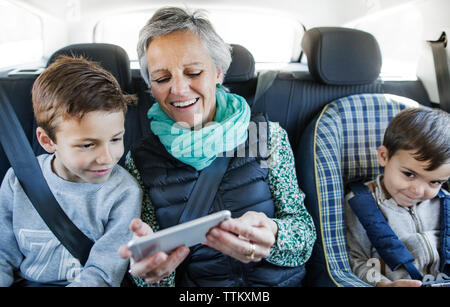 Felice donna senior utilizzando smart phone con nipoti in auto Foto Stock