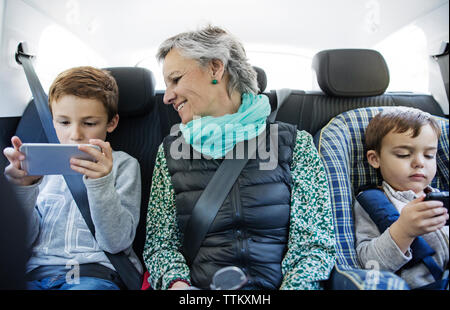 Senior donna che guarda la nipote utilizzando smart phone in auto Foto Stock