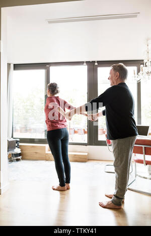 Uomo senior di aiutare la donna a fare yoga a casa Foto Stock
