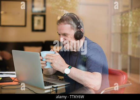 Felice l'uomo anziano avente il caffè mentre si ascolta la musica tramite portatile a casa Foto Stock