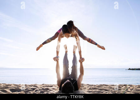 Uomo Donna di sollevamento mentre fa yoga sulla spiaggia durante la stagione estiva Foto Stock