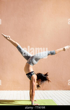 Determinata giovane donna con gambe divaricate facendo handstand sul marciapiede Foto Stock