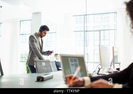 uomo d'affari che utilizza un tablet mentre i colleghi lavorano in ufficio Foto Stock