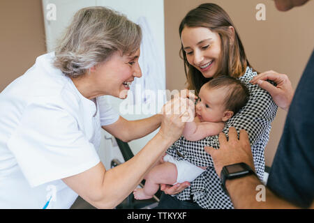 Madre sorridente guardando medico gioca con baby boy in sala esame Foto Stock