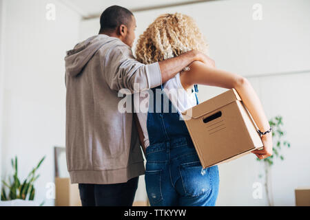 Vista posteriore della donna che la porta box in piedi con il marito a casa nuova Foto Stock