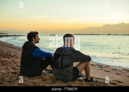 Considerato il padre e il figlio in appoggio durante la seduta t beach contro sky durante il tramonto Foto Stock