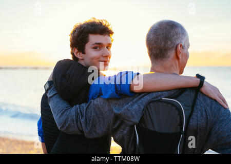Ritratto di fiducioso figlio con il braccio intorno al padre la spalla alla spiaggia Foto Stock