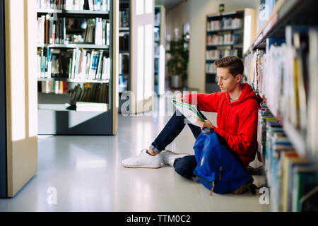 L uomo lo studio mentre è seduto sul pavimento in libreria Foto Stock