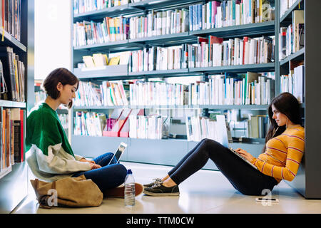 Amici di sesso femminile studi tramite computer portatile mentre è seduto sul pavimento in libreria Foto Stock