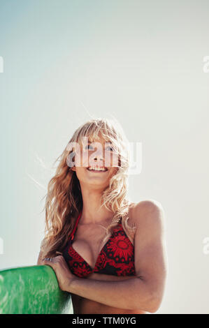 Considerato giovane donna che trasportano le tavole da surf contro il cielo chiaro Foto Stock