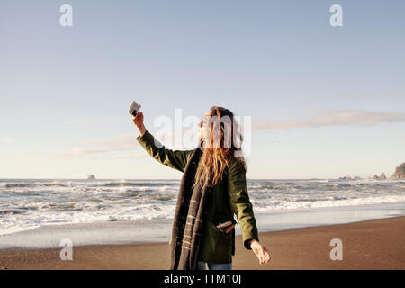 Vista laterale della donna fotografando attraverso smart phone sulla spiaggia Foto Stock