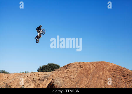 Basso angolo vista del biker eseguendo stunt contro il cielo blu chiaro Foto Stock