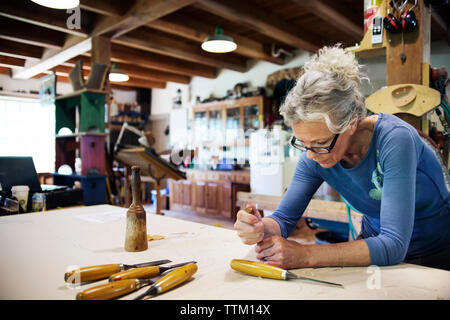 Femmina concentrato utilizzando uno scalpello per sagomare il legno in officina Foto Stock