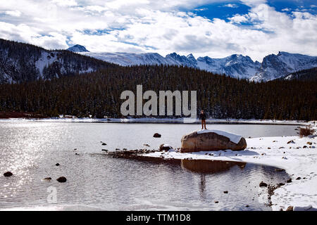 Uomo in piedi sulla roccia dal lago contro la montagna durante il periodo invernale Foto Stock