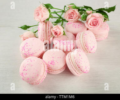 Gustosi amaretti con bellissime rose sul tavolo di legno Foto Stock