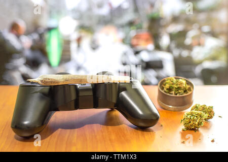 Video giochi e la cannabis. Video controller di gioco, grande e comune di Mola con boccioli di marijuana su un tavolo di legno. La sfocatura sullo sfondo di un tv con video gioco. Foto Stock