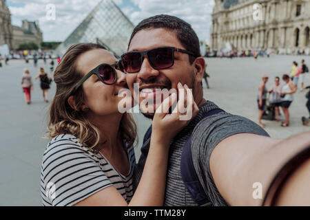 Ritratto di ragazza baciare Ragazzo contro il Musee du Louvre in città Foto Stock