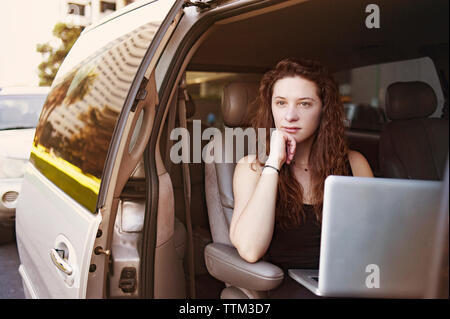 Considerato giovane donna seduta con il computer portatile in auto Foto Stock
