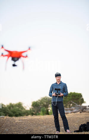 Lunghezza completa di uomo drone di funzionamento tramite telecomando contro il cielo chiaro Foto Stock