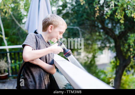 Giocoso ragazzo la spruzzatura di acqua con tubo flessibile da giardino mentre in piedi in balcone Foto Stock