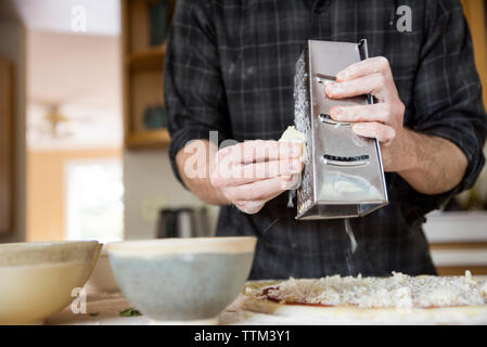 Sezione mediana dell'uomo grattugiare il formaggio sulla pizza sull Isola per cucina a casa Foto Stock