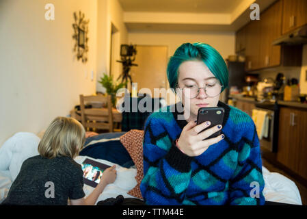 I fratelli utilizzando le tecnologie senza fili mentre vi rilassate sul letto di casa Foto Stock