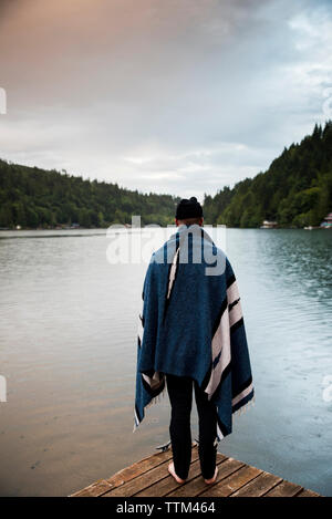 Vista posteriore dell'uomo con coperta guardando il lago mentre si sta in piedi sul molo contro sky nel Parco Nazionale di Olympic Foto Stock