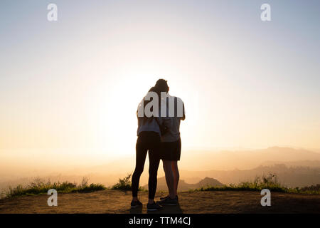 Vista posteriore del giovane permanente sulla montagna contro il cielo chiaro durante il tramonto Foto Stock
