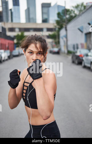 Ritratto di donna fiducioso il pugilato mentre si ascolta la musica su una strada di città Foto Stock