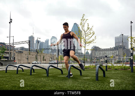 Per tutta la lunghezza della giovane uomo a scavalcare push-up bar a parcheggiare in città Foto Stock