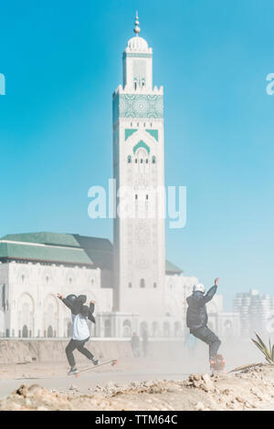 Lunghezza completa di amici lo skateboard contro la moschea Hassan II Foto Stock