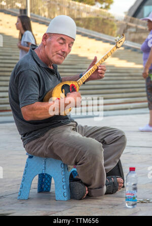 Uomo anziano riproduce la musica su un tradizionale. Strumento a corda,seduto fuori nel Vecchio Bazar area di Skopje. Foto Stock