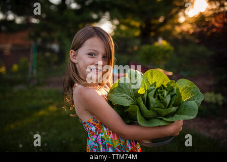 Felice ragazza che trasportano le lattughe in coppa a backyard Foto Stock