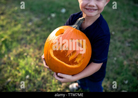 Sezione bassa di boy holding jack o lantern mentre si sta in piedi sul campo in cantiere Foto Stock