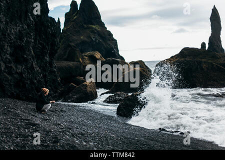 Vista laterale della donna accovacciata sul litorale di spiaggia contro sky Foto Stock