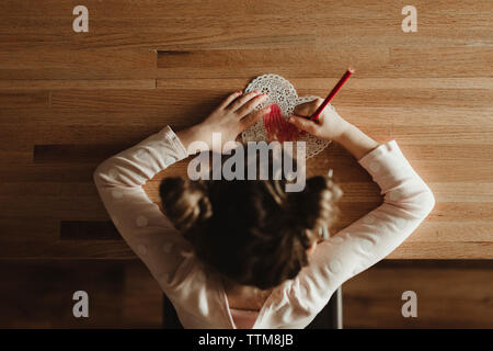Vista aerea della ragazza facendo valentine card sul tavolo a casa Foto Stock
