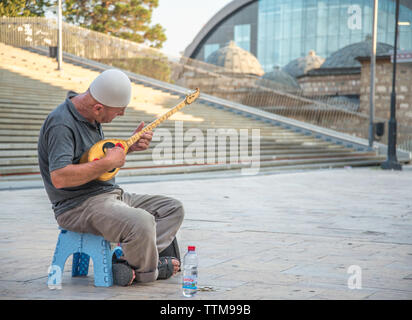 Uomo anziano riproduce la musica su un tradizionale. Strumento a corda,seduto fuori nel Vecchio Bazar area di Skopje. Foto Stock