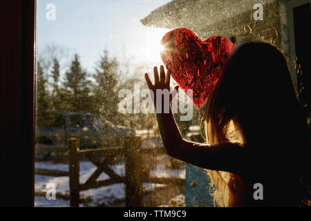 Ragazza disegno forma di cuore sulla finestra a casa Foto Stock