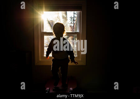 Silhouette ragazzo accanto a finestra in camera oscura a casa Foto Stock