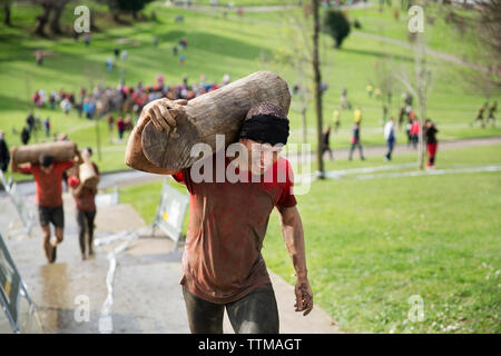 Elevato angolo di visione dell uomo che porta log e passaggi di arrampicata durante la gara Foto Stock