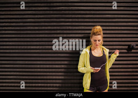 Atleta femminile ascoltare musica mentre è in piedi contro la parete ondulata Foto Stock