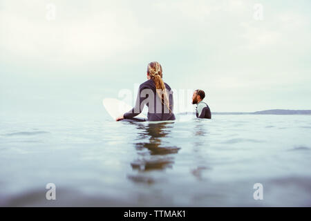 Maschio e femmina rilassante surfisti in mare contro il cielo nuvoloso Foto Stock