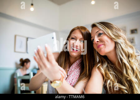 Allegro amiche tenendo selfie attraverso smart phone in cafe Foto Stock