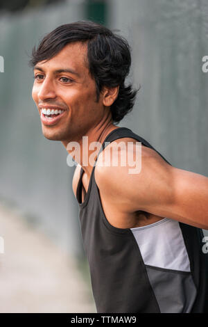 Montare il giovane uomo ridendo durante il warm up prima esecuzione di allenamento, Foto Stock