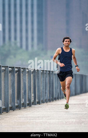 Giovane uomo corre lungo molo fronte mare nel ponte di Brooklyn Park Foto Stock